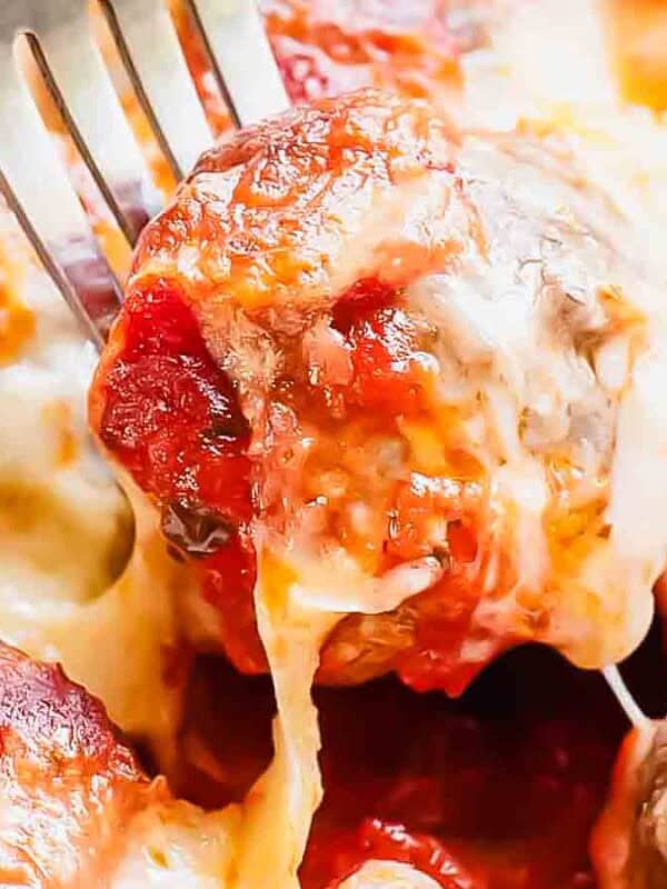 Close-up of a fork holding a cheesy, saucy meatball. The meatballs are covered in melted cheese and tomato sauce, nestled closely together, emitting a delicious and savory appearance.
