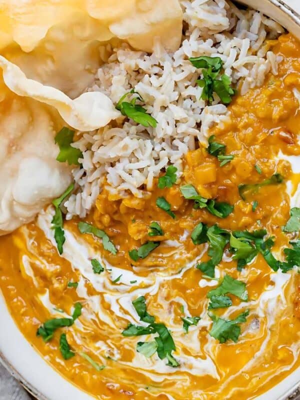 A bowl of yellow lentil curry topped with fresh cilantro, served with white rice and two crispy papadums, with a spoon and fresh cilantro on the side.