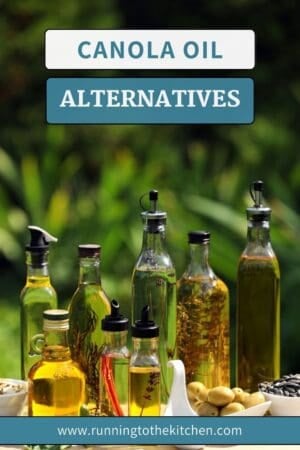 A variety of oil bottles, some filled with herbs, are arranged on a table outdoors with a green blurred background. Text on the image reads "Canola Oil Alternatives" and "www.runningtothekitchen.com".