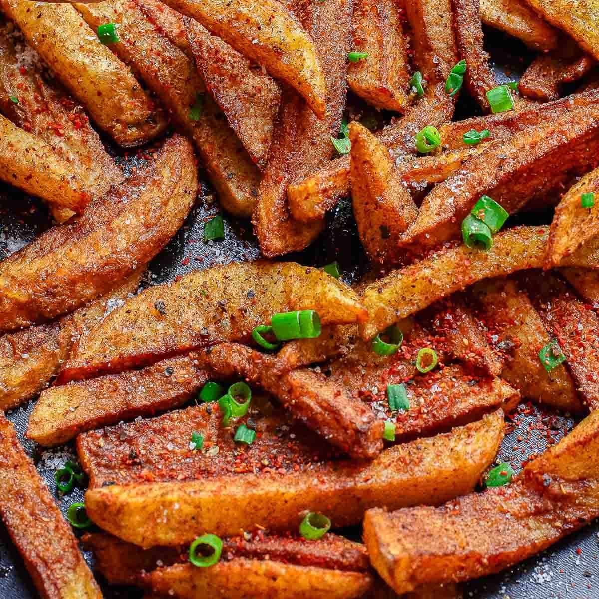 Close-up of crispy, masala seasoned potato fries garnished with chopped green onions and a sprinkle of spices.