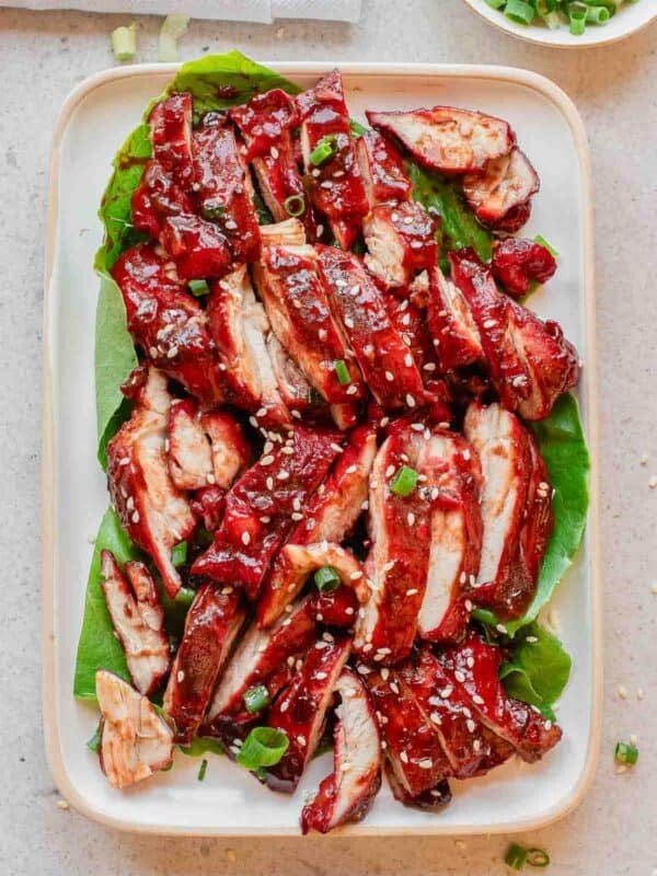 Sliced Chinese BBQ chicken (char siu) arranged on lettuce leaves, garnished with chopped green onions and sesame seeds, served on a rectangular white plate.
