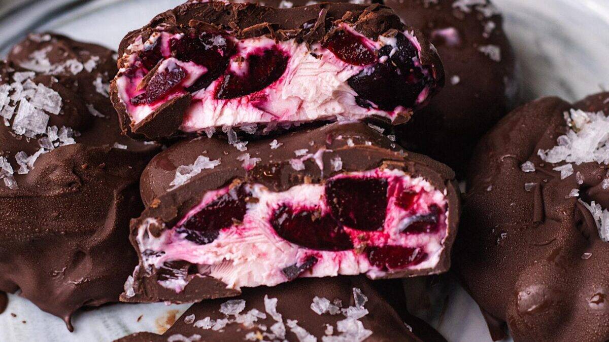 A close-up of chocolate-covered treats, cut open to reveal a creamy pink and red cherry filling, topped with flaky sea salt.