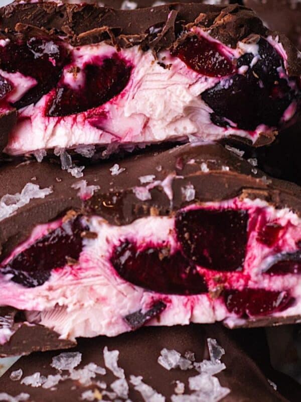 A close-up of chocolate-covered treats, cut open to reveal a creamy pink and red cherry filling, topped with flaky sea salt.