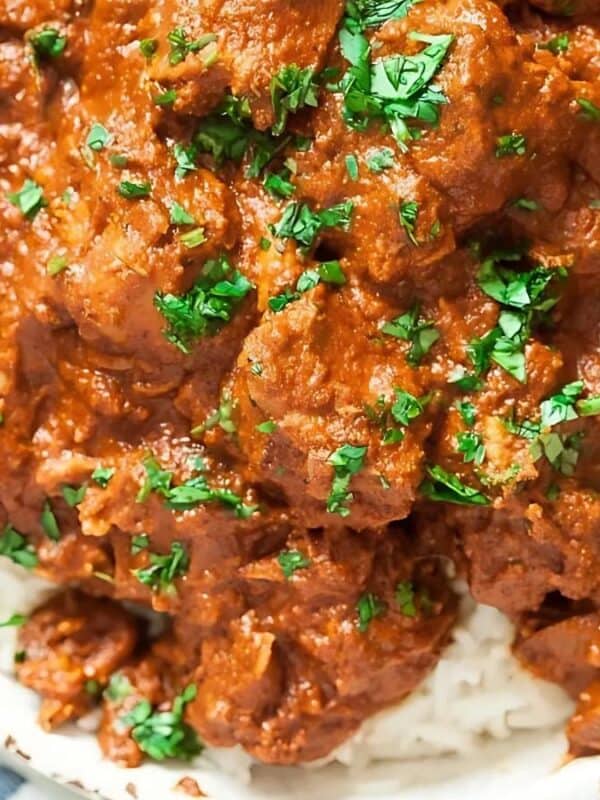 A bowl of white rice topped with rich, saucy beef curry, garnished with chopped fresh cilantro. A fork and napkin are visible to the side.