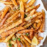 A plate of golden-brown parmesan truffle fries topped with chopped herbs, garnished with lemon wedges.