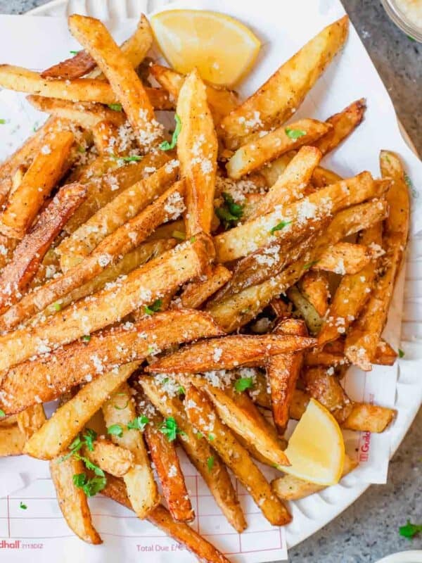 A plate of golden-brown parmesan truffle fries topped with chopped herbs, garnished with lemon wedges.