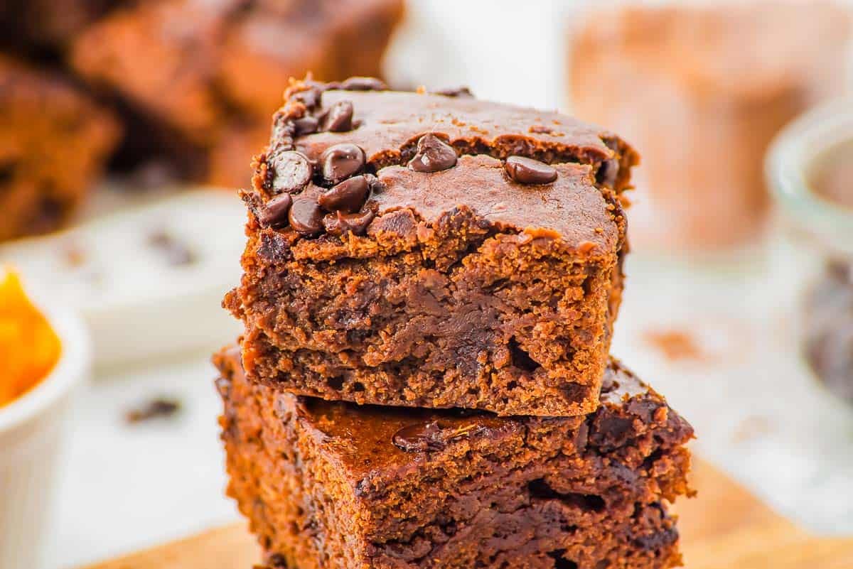 Two thick, fudgy chocolate sweet potato brownies studded with chocolate chips are stacked on top of each other. The brownies have a moist texture and a rich, dark brown color.