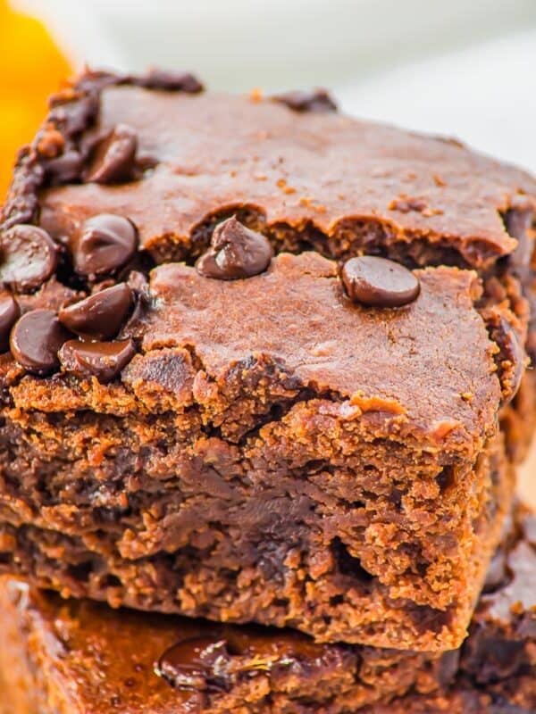 A close-up of two fudgy, chocolate chip sweet potato brownies stacked on top of each other, showing a moist, rich texture and scattered chocolate chips on top.