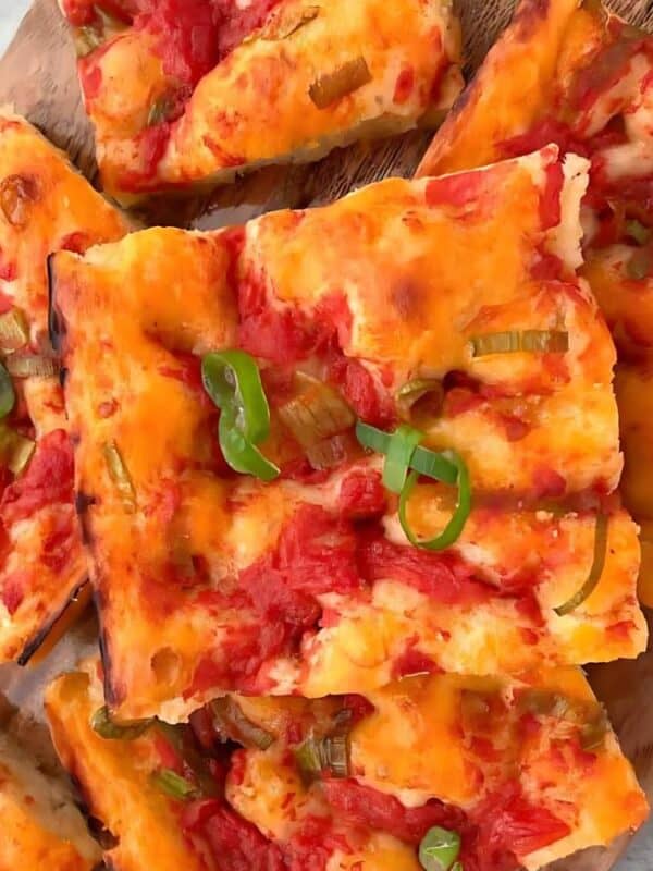 Slices of rectangular pizza with tomato sauce, melted cheese, and chopped green onions on top, arranged on a wooden serving board.