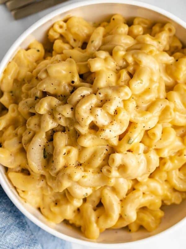 A bowl of creamy macaroni and cheese topped with black pepper, placed on a light surface with a blue napkin nearby.