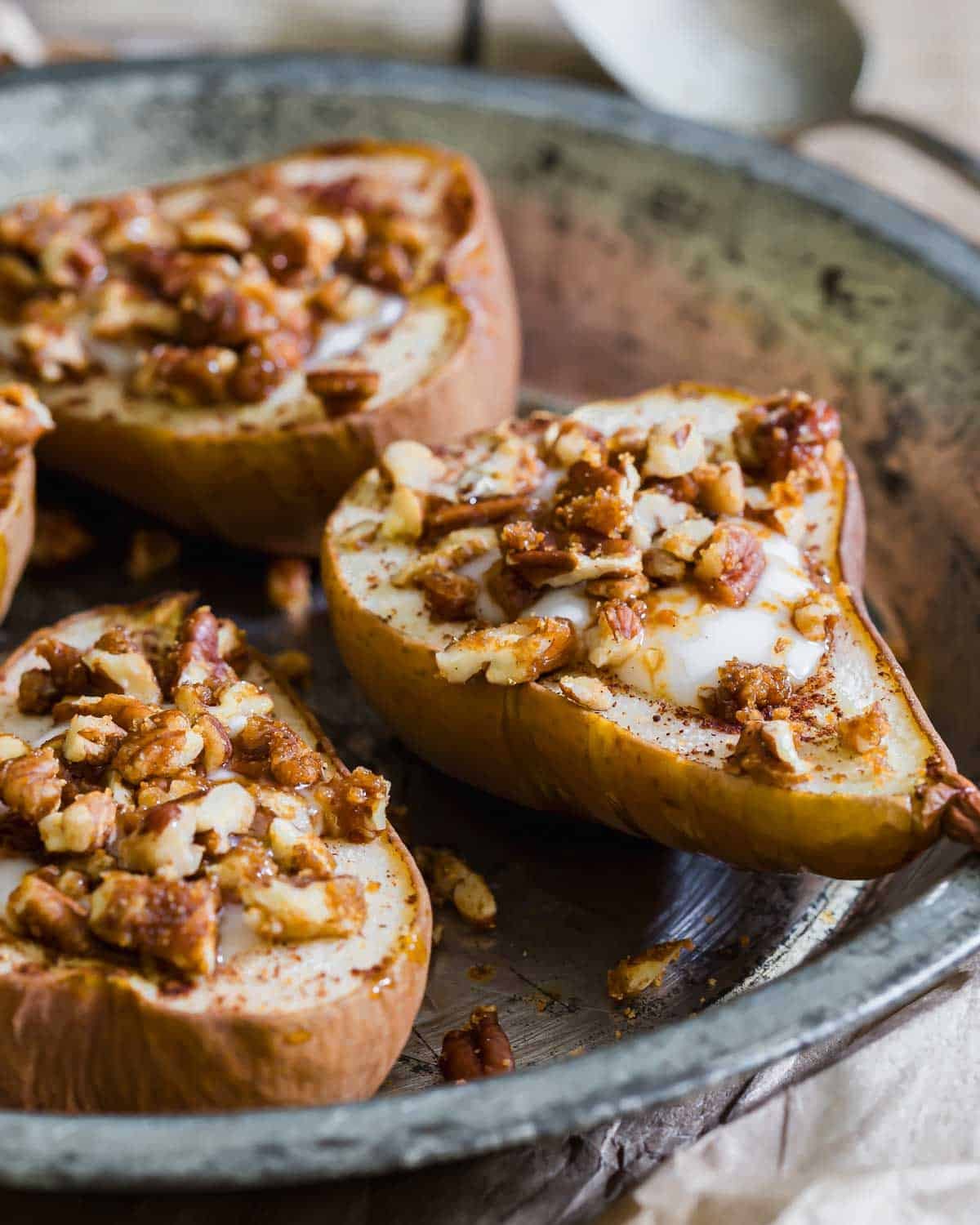Baked pear halves topped with chopped nuts, brown sugar, and a dollop of cream, served in a rustic metal dish.