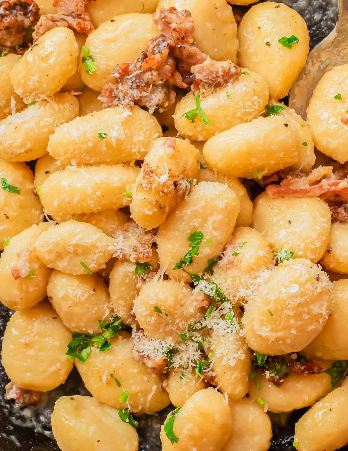 A close-up of creamy gnocchi carbonara topped with grated cheese, bits of bacon, and chopped parsley.