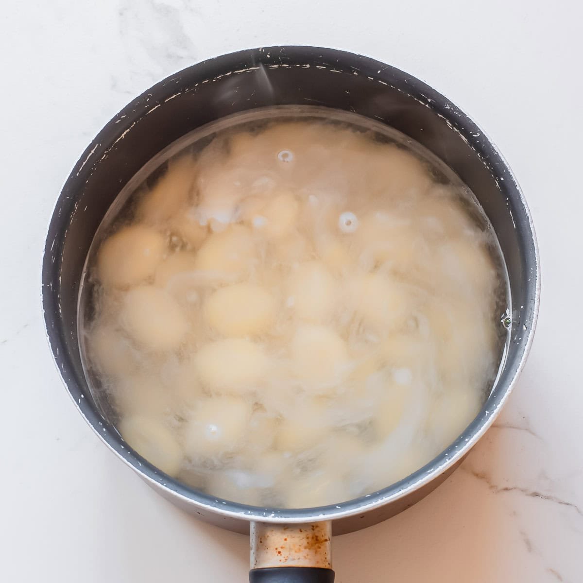 A pot filled with gnocchi boiling in water on a white surface. Steam is visible rising from the water.