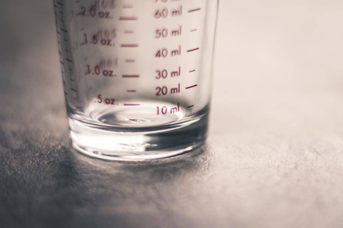 A close-up of a clear glass measuring cup on a gray surface, showing red measurement markings in milliliters and ounces, with the numbers clearly visible and the focus on the lower part of the cup.