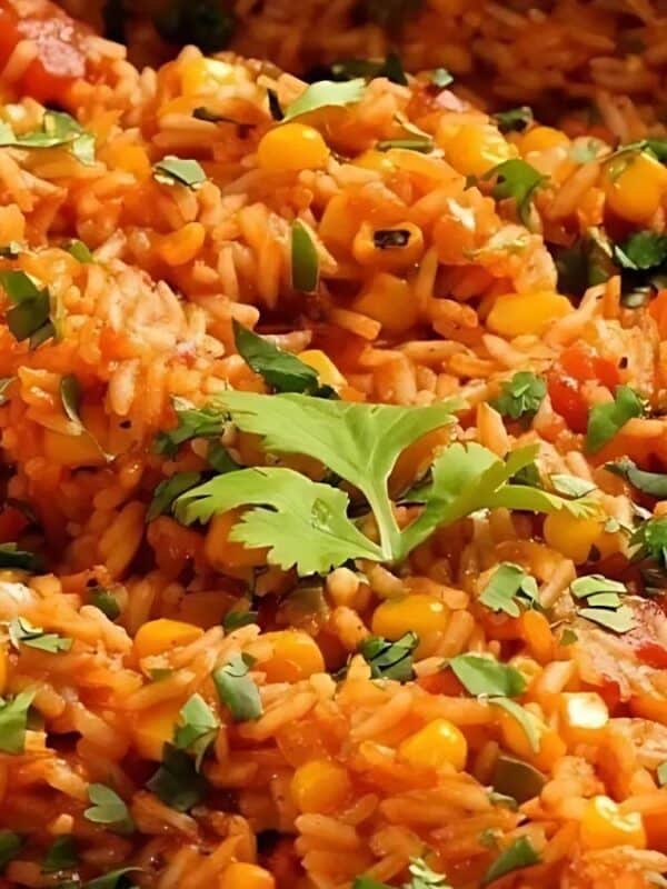 A close-up of Mexican rice with corn, tomato sauce, and chopped cilantro, with a wooden spoon partially visible on the left side.