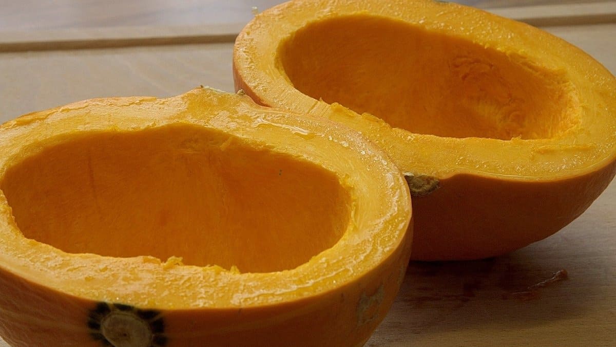 Two halves of a hollowed-out orange pumpkin are placed on a wooden surface, showing their smooth, bright orange flesh and empty centers where the seeds have been removed.