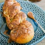 A pretzel twist is drizzled with caramel sauce sitting on a blue patterned plate, with a spoon and a jar of sauce in the background.