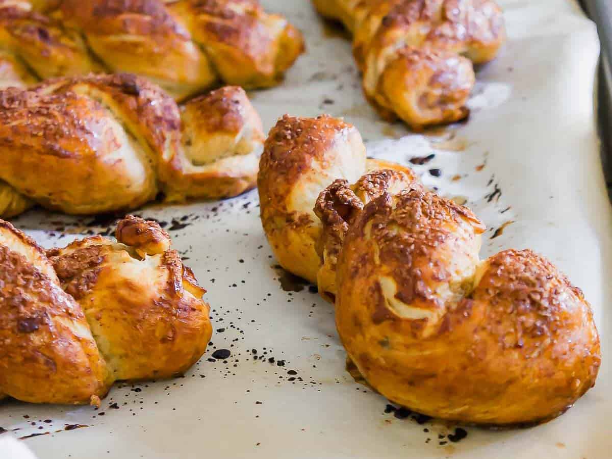 Golden-brown twisted baked goods on parchment paper with dark specks, on a baking sheet.