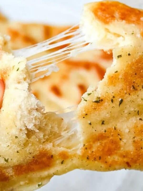Close-up of hands pulling apart a piece of golden, pan-fried bread with melted, stretchy cheese inside and flecks of herbs on the crust.