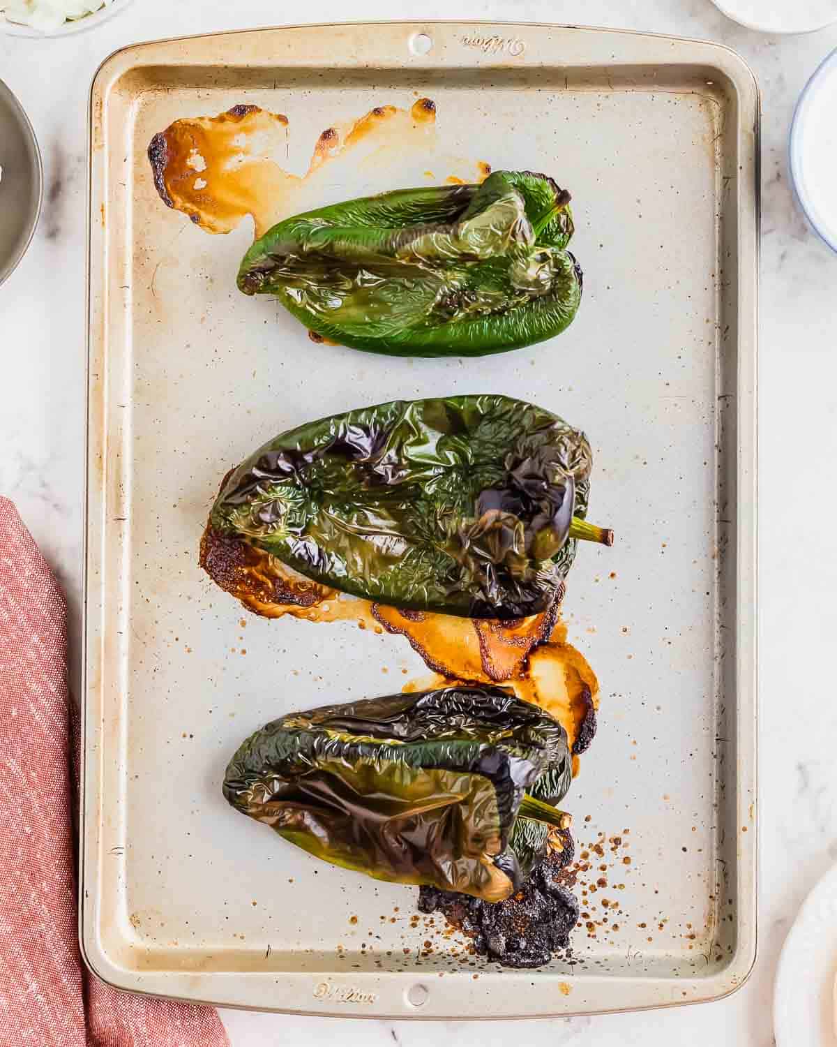 A tray of roasted poblano peppers on a baking sheet.