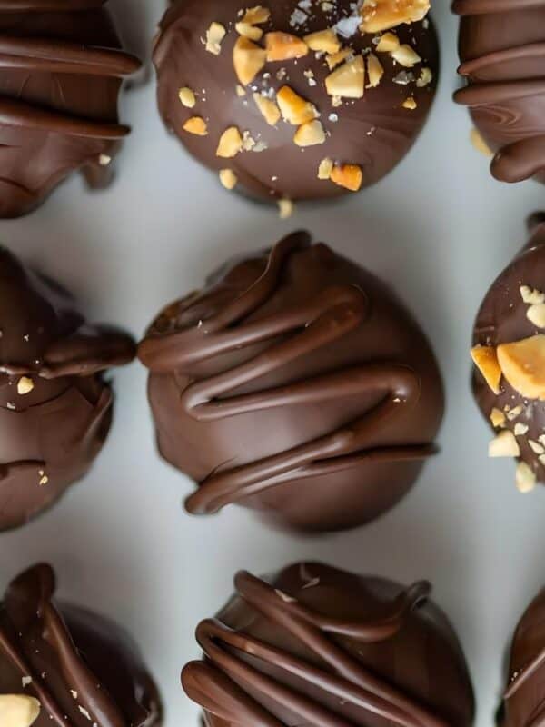 A close-up of rows of round chocolate truffles, some topped with chopped nuts and others drizzled with dark chocolate, arranged neatly on a white surface.