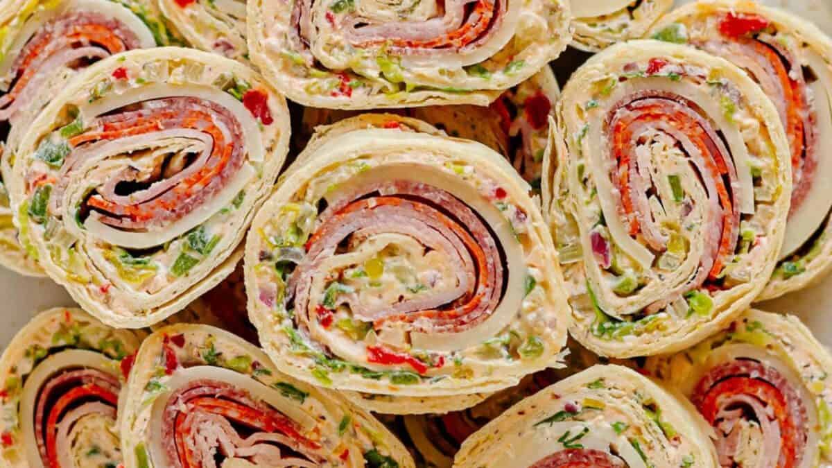 Close-up of several tortilla pinwheels filled with layers of deli meats, cheese, chopped vegetables, and cream cheese, sliced and stacked together, showing colorful spirals.