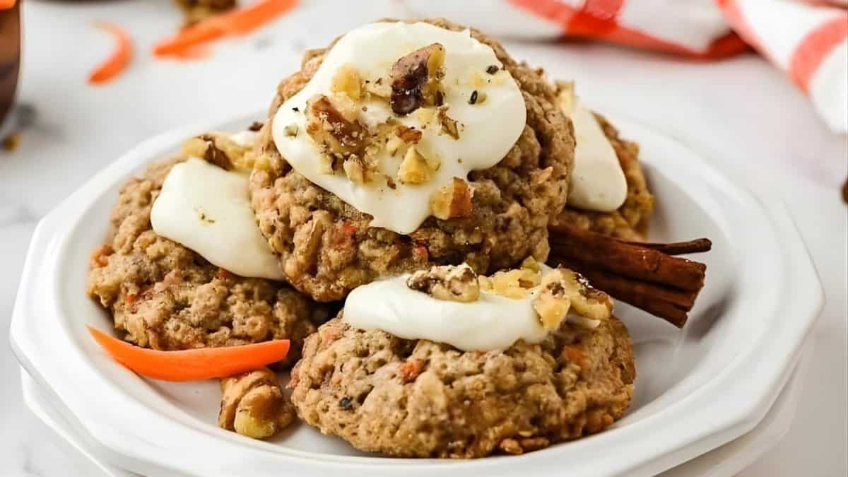 A white plate with four oatmeal cookies topped with white icing and chopped nuts, garnished with cinnamon sticks and an orange peel on a white surface.