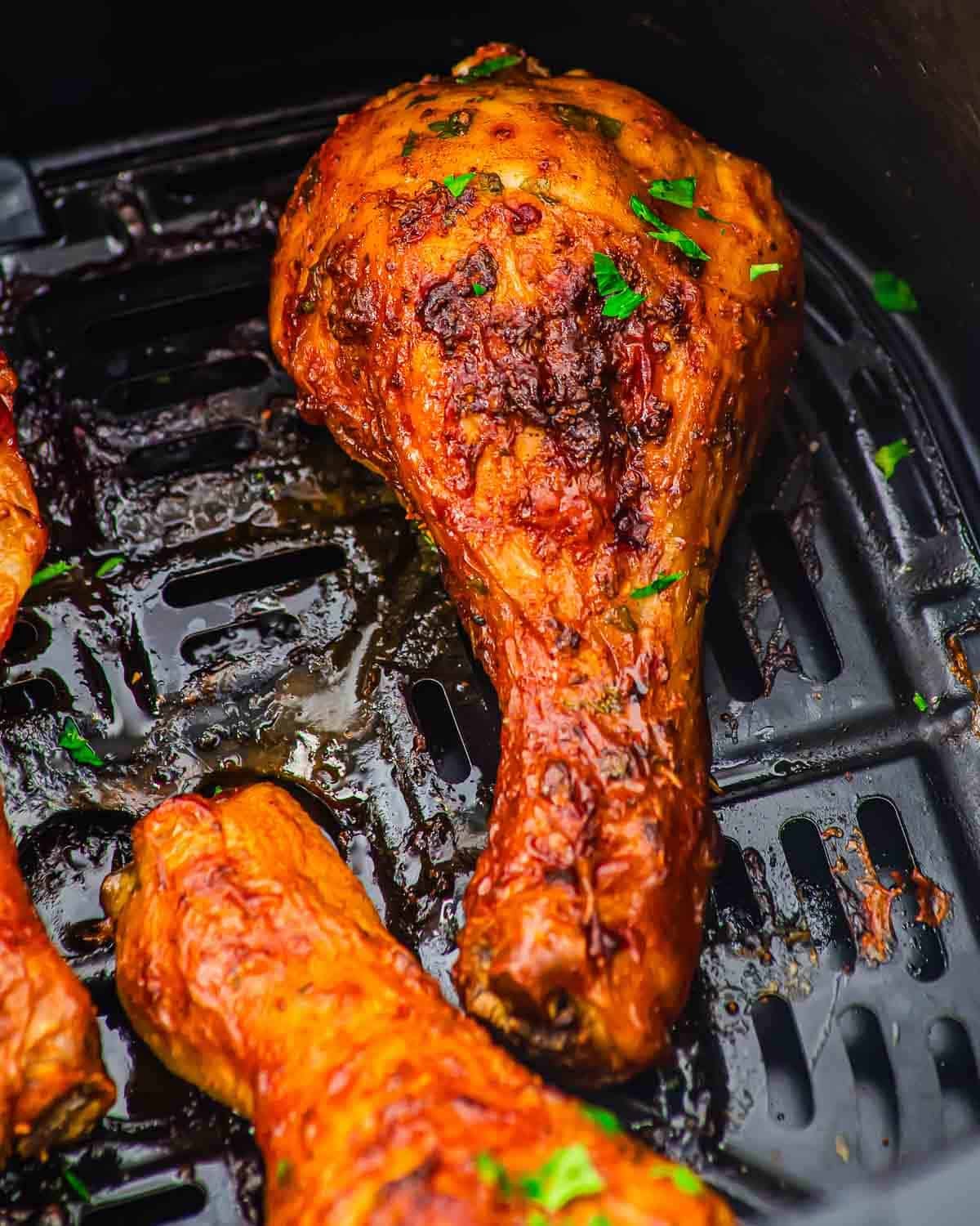 Close-up of a crispy, golden-brown roasted chicken leg in an air fryer basket, garnished with chopped parsley.