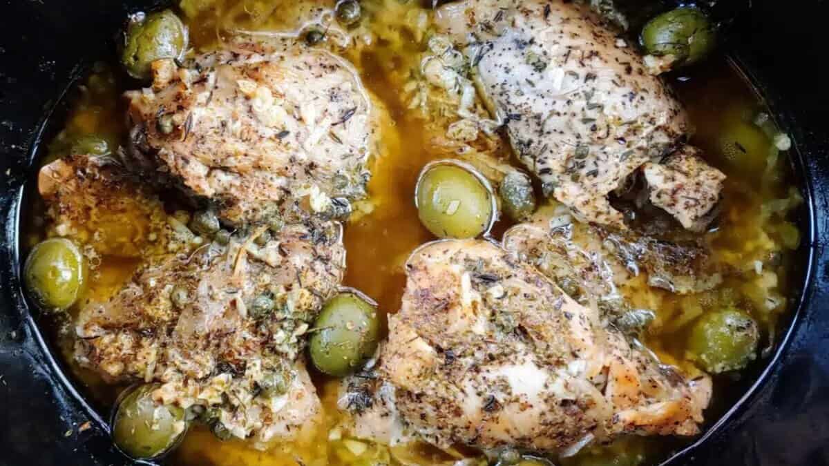 Four pieces of herb-seasoned chicken cooked in a savory broth with green olives and capers, garnished with herbs and spices.