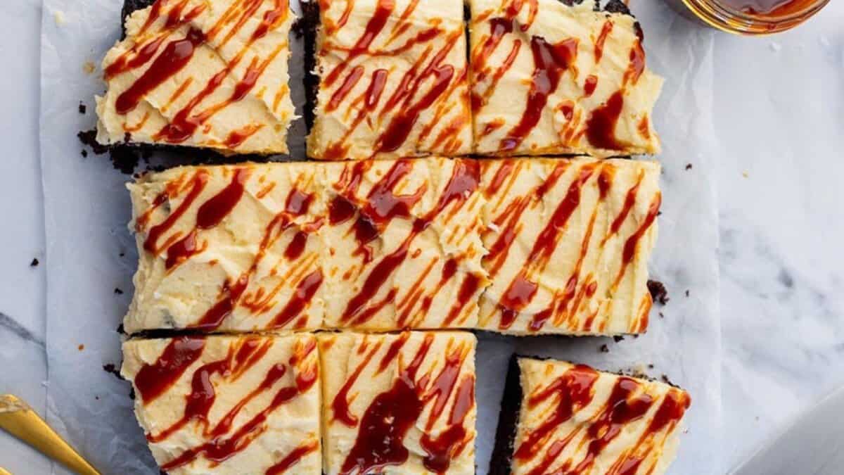 Nine rectangular pieces of frosted cake on parchment paper, topped with caramel drizzle. The cake is cut into squares, and some pieces are slightly separated. The background is a marble surface.
