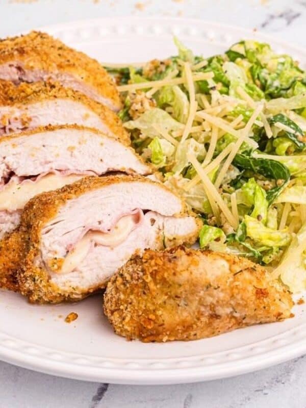 A white plate with sliced breaded chicken breast—an Easy Dinner inspired by Air Fryer Chicken Recipes—and a side of green salad topped with shredded cheese, set on a light marble surface with a fork and knife nearby.