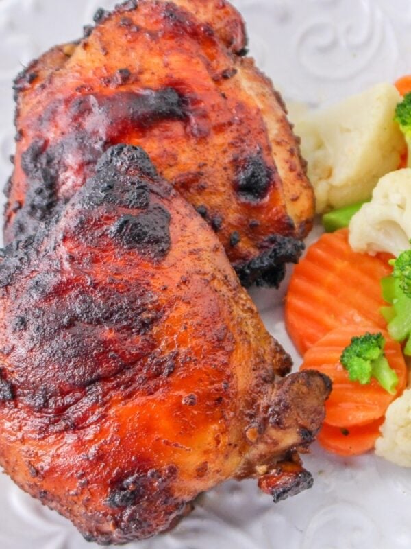 A white plate with two pieces of juicy grilled chicken, perfect for weeknight chicken recipes, and a side of steamed mixed vegetables—broccoli, cauliflower, and sliced carrots. A fork and napkin are on the table beside the plate.