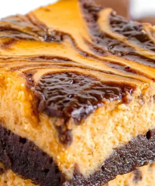 Two stacked dessert bars with a thick, fudgy chocolate base and a creamy, marbled orange and brown topping—likely pumpkin and chocolate swirled together—these irresistible brownies boast a rich, moist texture that will tempt anyone to bake brownies at home.