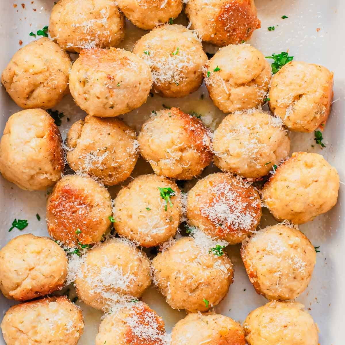 A tray filled with golden-brown baked chicken meatballs, sprinkled with grated parmesan and chopped parsley.