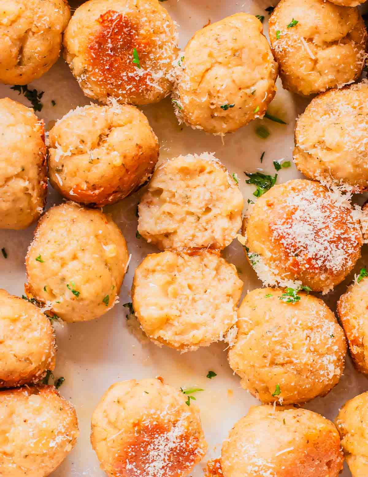 Golden brown baked chicken meatballs in a baking dish sprinkled with grated parmesan cheese and chopped parsley for garnish. One meatball is sliced in half in the center.