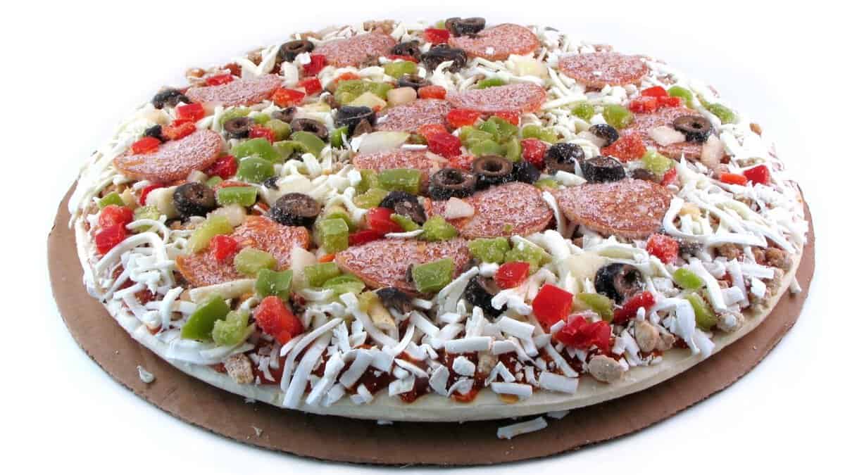 A frozen pizza featuring shredded cheese, pepperoni slices, black olives, green and red bell peppers, and diced onions on a round cardboard tray&mdash;a delicious nod to current food trends.