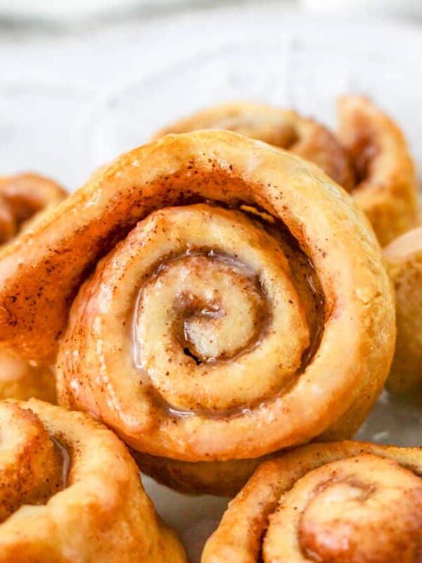Close-up of several sweet crescent rolls on a white plate, showing their golden-brown swirled layers and melted icing.