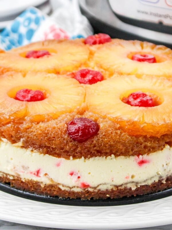 A pineapple upside-down cheesecake topped with pineapple rings and cherries sits on a white plate, showcasing one of the Instant Pot cheesecakes perfect for your dessert table, with colorful napkins in the background.