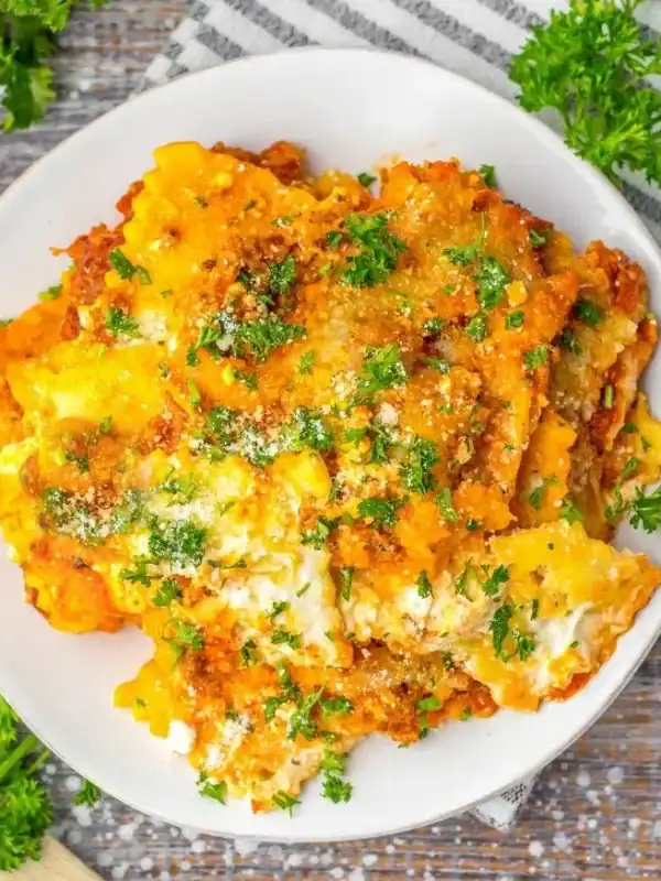 A plate of cheesy baked lasagna, one of the most comforting casseroles, garnished with chopped parsley, set on a rustic wooden table with a striped napkin, grated cheese in a small bowl, and fresh parsley nearby.