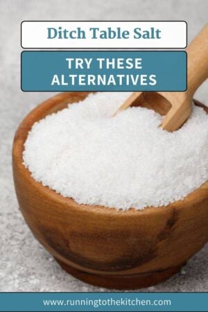 A wooden bowl filled with coarse salt and a small wooden scoop, with text above reading "Ditch Table Salt: Try These Salt Alternatives" and a website link at the bottom.