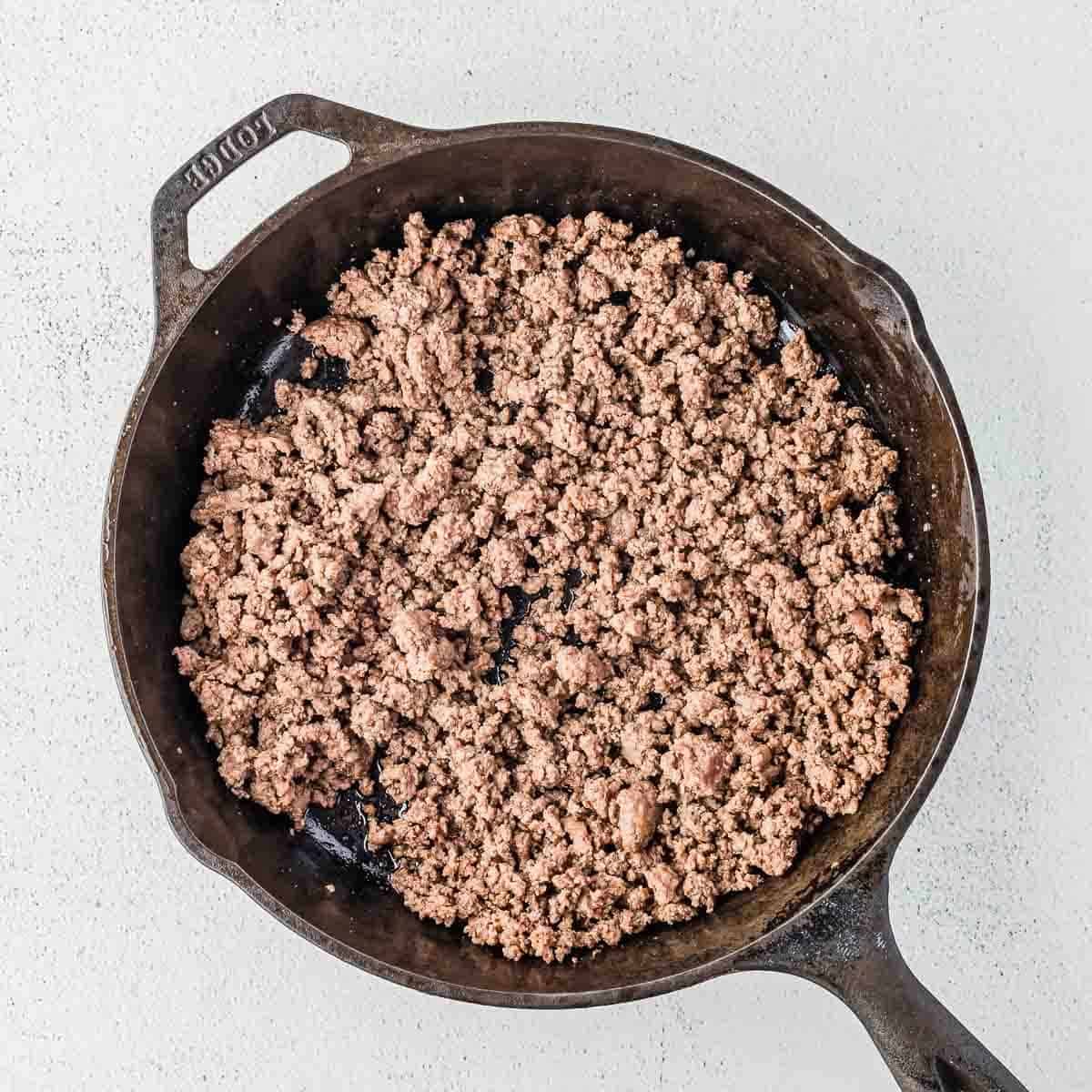 Cooked ground beef in a black cast iron skillet, displayed on a light-colored surface.
