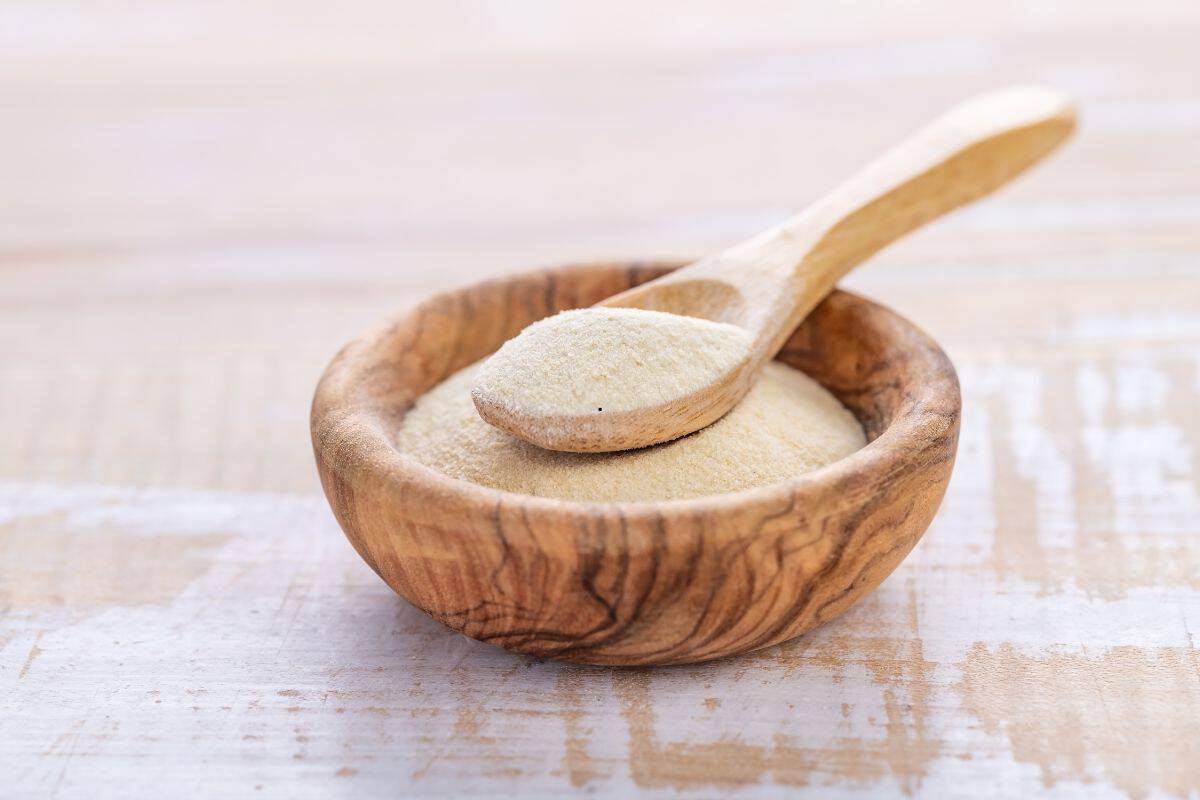 A small wooden bowl filled with a light beige powder, a popular substitute for cornstarch, with a wooden spoon resting on top containing the same powder, placed on a light wooden surface.