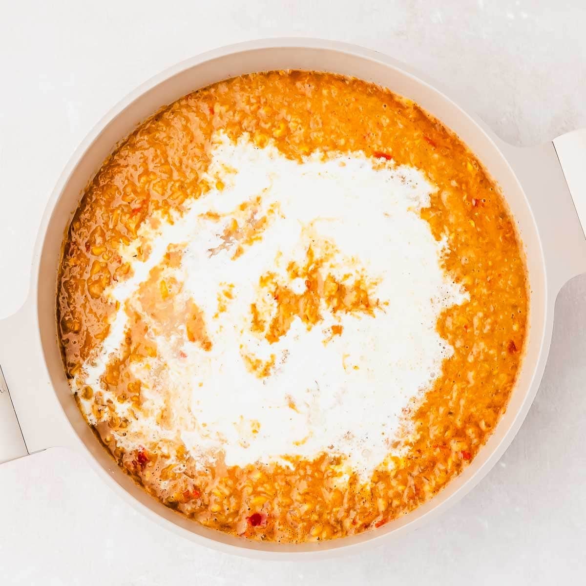A pot of creamy street corn soup, topped with a swirl of cream, photographed from above on a light background.