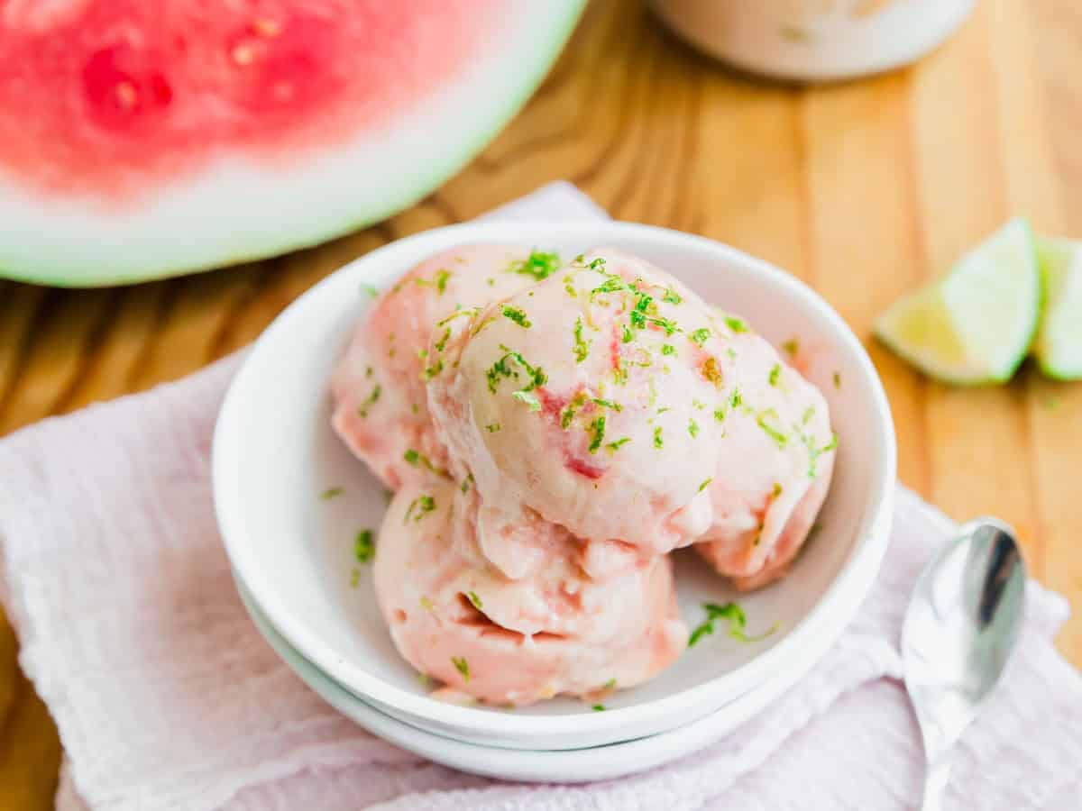 Watermelon ice cream scoops garnished with lime zest in a white bowl.