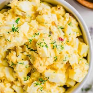 A close-up of a bowl filled with cottage cheese egg salad garnished with fresh dill. The salad contains chopped eggs, mayonnaise, and herbs, and is placed on a light-colored surface.