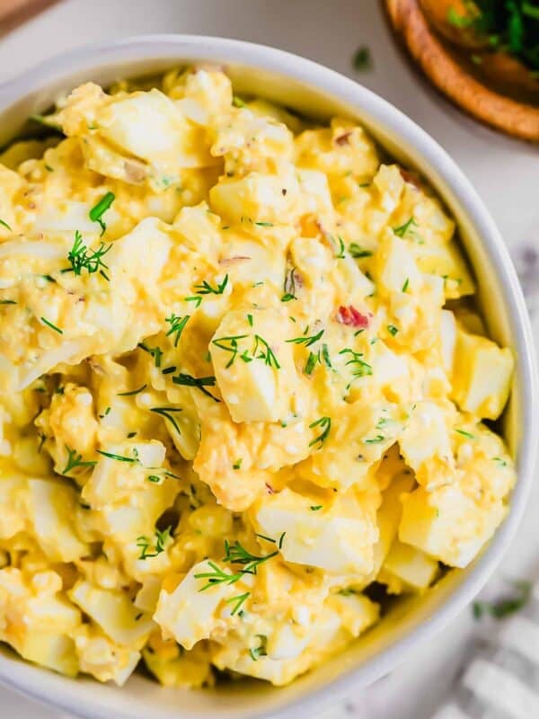 A close-up of a bowl filled with cottage cheese egg salad garnished with fresh dill. The salad contains chopped eggs, mayonnaise, and herbs, and is placed on a light-colored surface.