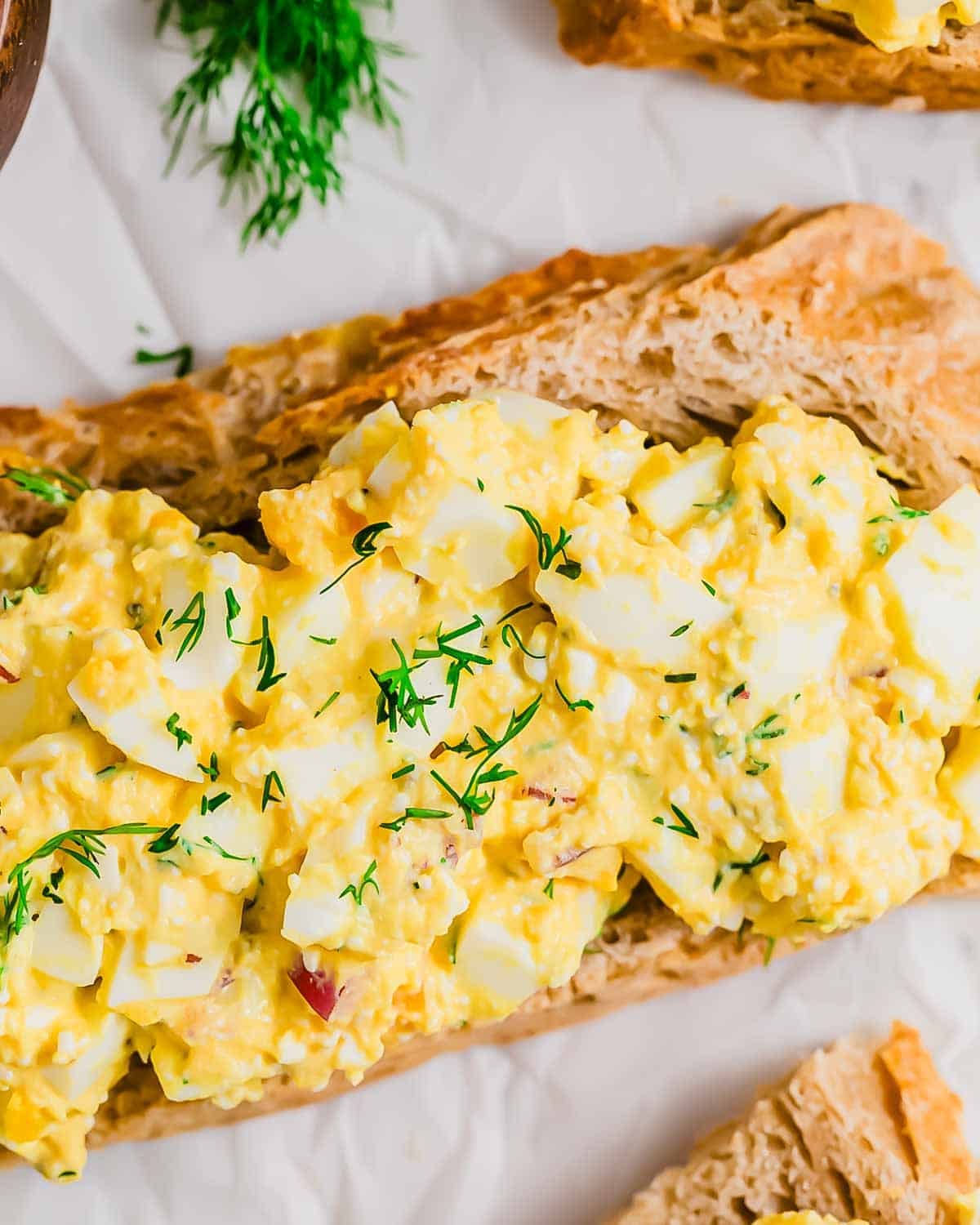 Close-up of an open-faced high-protein cottage cheese egg salad sandwich on rustic bread, garnished with fresh dill, shown from above.