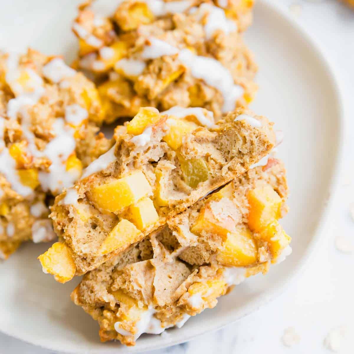 A close-up of the inside of baked peach fritters drizzled with white icing, shown on a white plate.