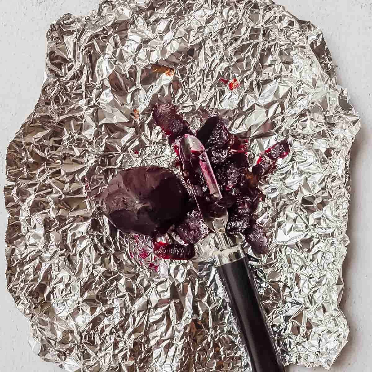 A peeled roasted beet with a peeler rests on a crumpled sheet of aluminum foil.