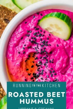 A bowl of bright pink beet hummus topped with black sesame seeds and olive oil, with cucumber slices and crackers on the side. Text overlay reads: “Roasted Beet Hummus - Vibrant & Creamy!”.